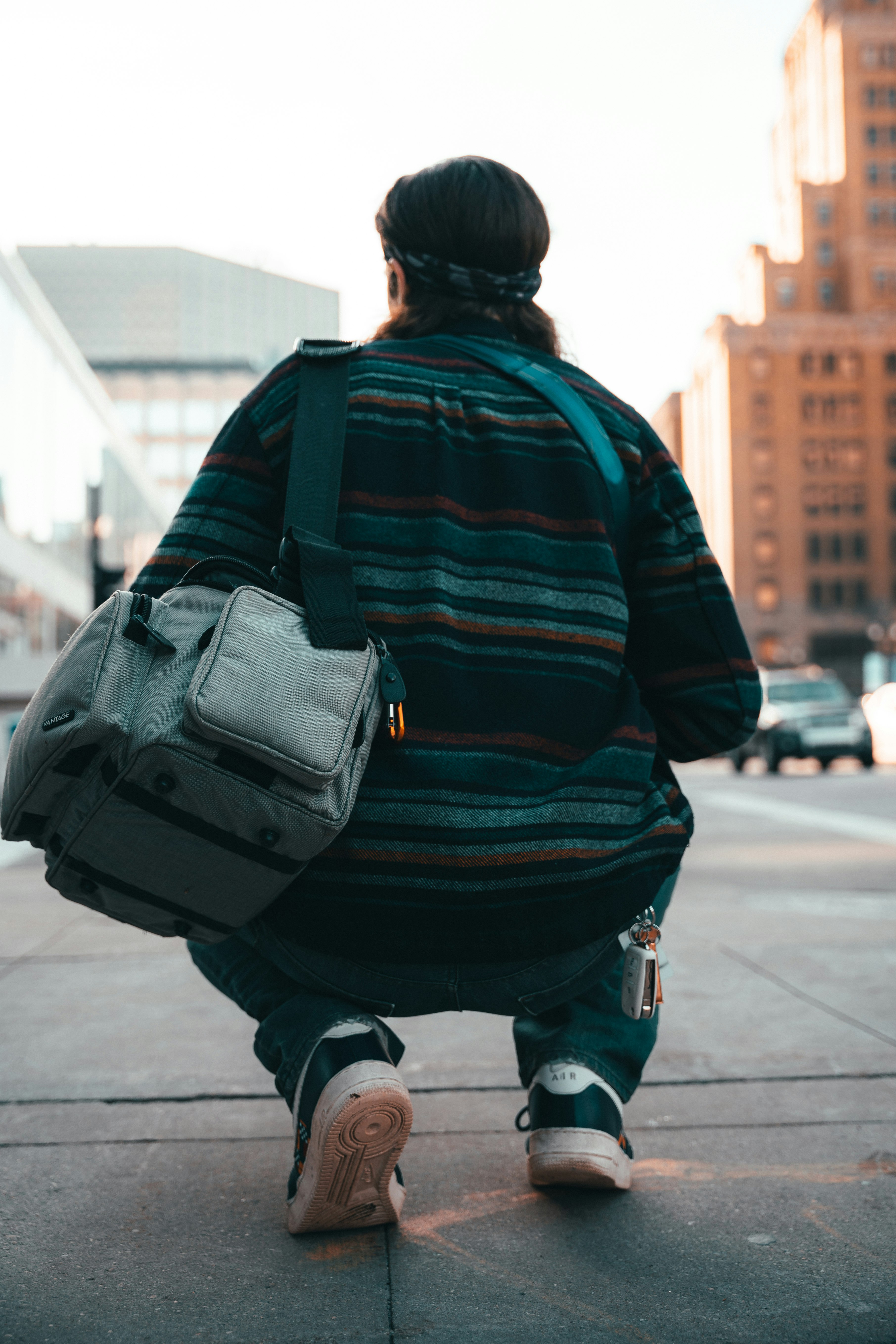 man in black and red jacket carrying black backpack walking on sidewalk during daytime